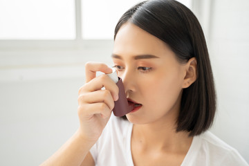 Asian Woman having asthma using the asthma inhaler for being healthy on her bed in bedroom - obrazy, fototapety, plakaty