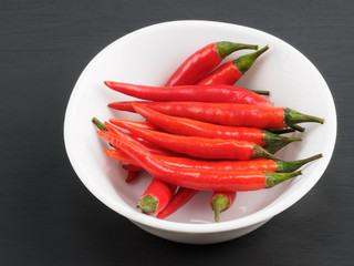 Red chili pods in white bowl on black wooden background