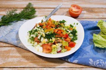 fresh vegetable salad in white plate on textile cover on wooden background with ingredients