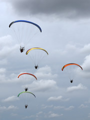 A group of colorful powered paragliders flying in the blue sky with clouds in the background
