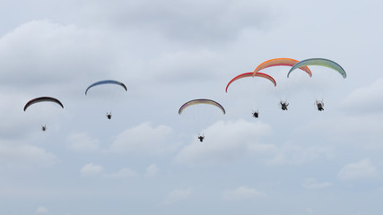 A group of colorful powered paragliders flying in the blue sky with clouds in the background