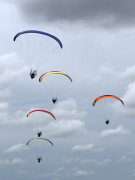 A group of colorful powered paragliders flying in the blue sky with clouds in the background