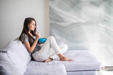 Happy young woman relaxing on the sofa eating salad in her living room