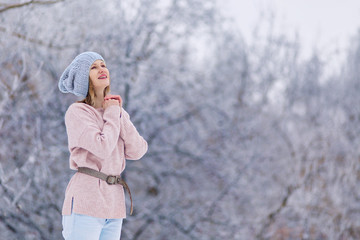 winter mood. A woman in  winter funny hat looks up. Walk December January February. Snowy tree  branches park walk. Beautiful girl in pink sweater. Place for text banner. dreams magic fairy tale