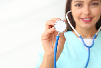 Female cardiologist with stethoscope on light background, closeup
