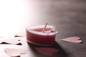 A heart-shaped candle in pink and paper hearts made of soft pink paper on a gray background. Symbol of Valentine's day. Selective focus.