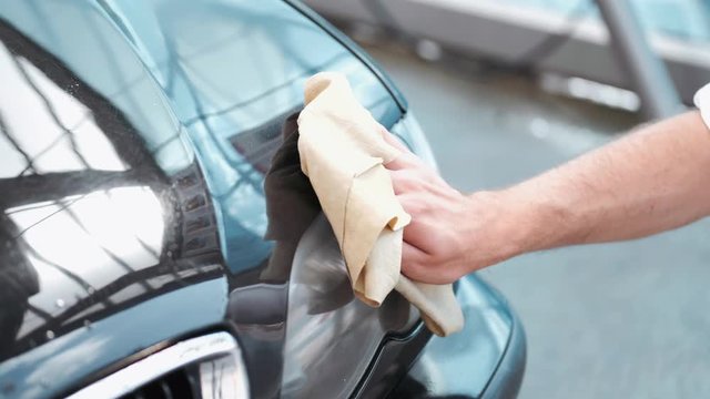A person is holding the cloth. A car is black. The man is washing his car.