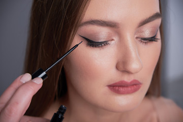 Make-up artist brush black eyeliner on the face of the woman. Young beautiful woman applying make-up by make-up artist