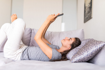 Pretty young woman lying on the couch and texting with smartphone