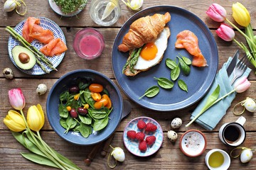 Easter festive brunch or breakfast set, meal variety with fried egg, asparagus, smoked salmon, salad bowl, avocado, croissant and smoothie. Flat layot
