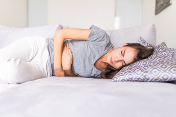 Young woman have abdominal pain because of menstruation lying in couch and holding her stomach.