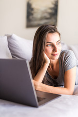 Fototapeta premium Smiling young woman laying on couch and using laptop
