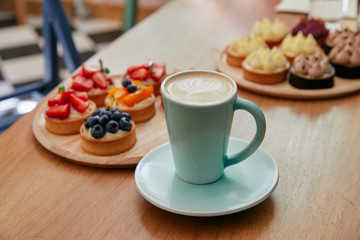 a white cup with a coffee is on a saucer, next to a plate are cupcakes with berries