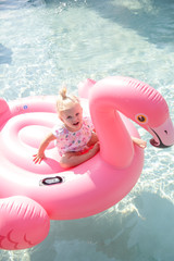 Adorable toddler girl having fun day at the pool and playing with big pink inflatable flamingo