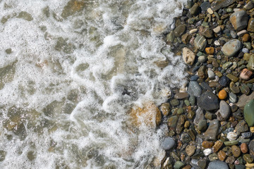 Sea water with foam on a pebble beach.