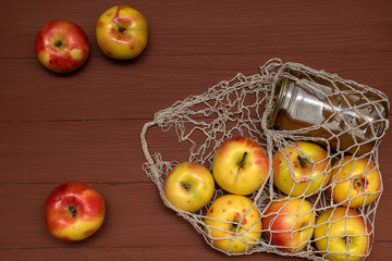 apples from a store and a jar of jam in a white grid lie on a brown wooden table