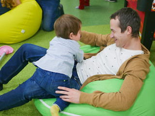 Young father with his son in the playroom. Happy young father plays with his cute little smiling son in a playroom on balloons and on a childrens slide