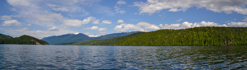 The dense pine forest lining the edges of Clearwater Lake reflects on the rippled water. The clouds and trees reflect on the surface of the lake on this calm and sunny day.