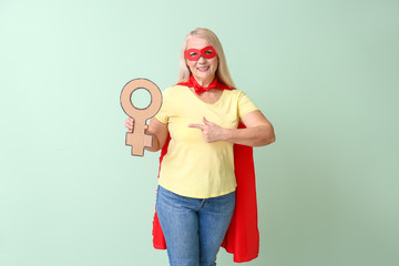 Lady in superhero costume holding symbol of woman on color background. Concept of feminism