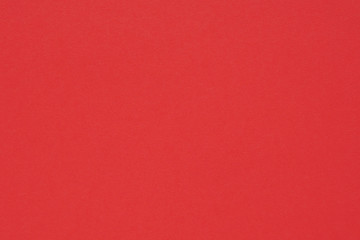 Red colored paper. Bright saturated background or wallpaper. Surface irregularities, spots and pores. View from above
