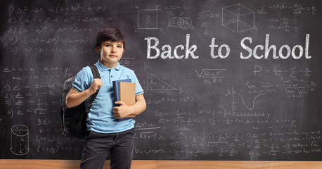 Boy with books posing in front of a chalkboard with text back to school and math formulas