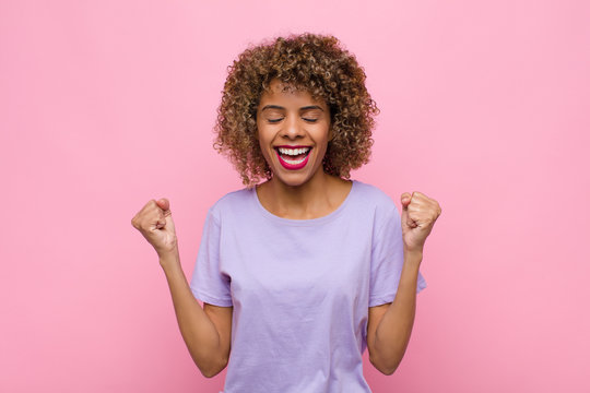 young african american woman looking extremely happy and surprised, celebrating success, shouting and jumping against pink wall
