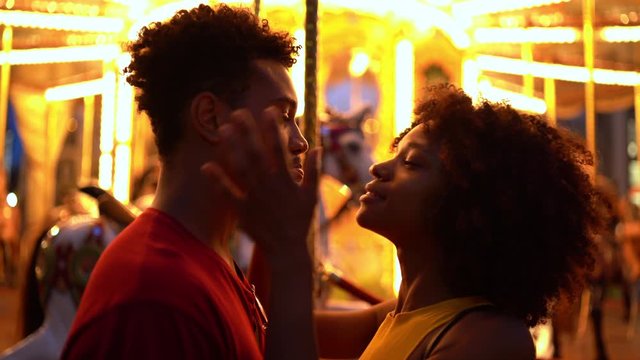 Young woman kissing sulking boyfriend at funfair