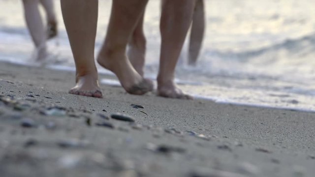 People walking barefoot on a beach with waves splashing feet and pebble stones