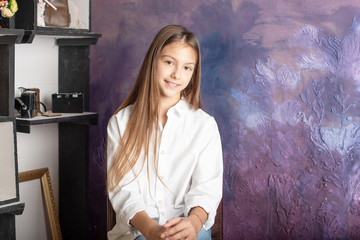 pretty teenage girl brunette with long hair stands against a purple wall, the concept of youth and natural female beauty, a girl in a white shirt