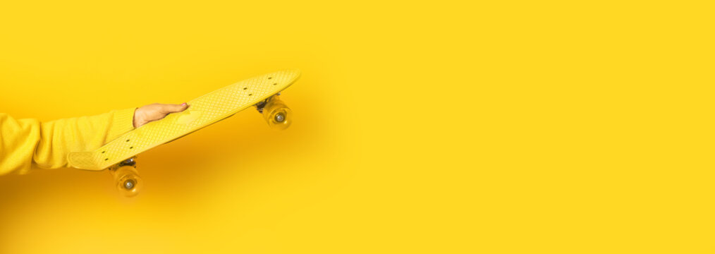 hand holding yellow  skate board over yellow background, panoramic mock up image