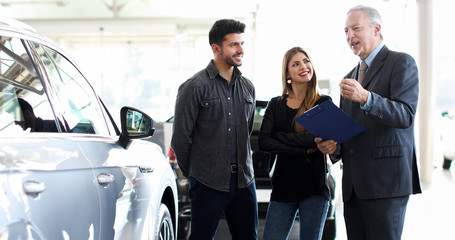 Car dealer exaplining a car's features to a couple by reading a document