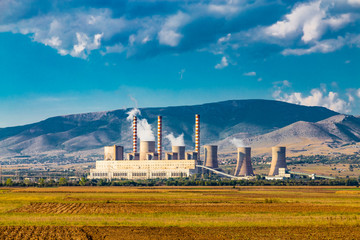Fototapeta na wymiar Steaming coal power plant over yellow agriculture field on the mountains background. Еnvironmental pollution concept.