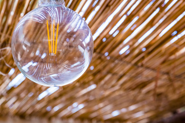 Modern energy saving filament led bulb edison style light lamp in a country tropical house with a thatched roof, modern technology, ecology concept.