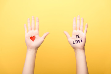 cropped view of woman showing palms with heart and is love lettering isolated on yellow