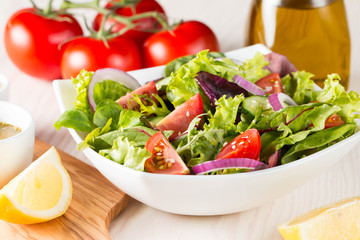 Fresh healthy salad with delicious ruccola, spinach, cabbage, arugula, feta cheese, red onion, cucumber, sesame seeds and cherry tomato on wooden background. Healthy and diet food concept.
