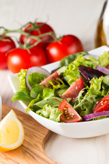 Fresh healthy salad with delicious ruccola, spinach, cabbage, arugula, feta cheese, red onion, cucumber, sesame seeds and cherry tomato on wooden background. Healthy and diet food concept.