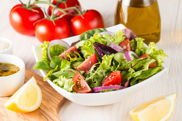 Fresh healthy salad with delicious ruccola, spinach, cabbage, arugula, feta cheese, red onion, cucumber, sesame seeds and cherry tomato on wooden background. Healthy and diet food concept.
