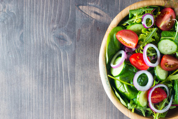 Fresh healthy salad with delicious ruccola, spinach, cabbage, arugula, feta cheese, red onion, cucumber, sesame seeds and cherry tomato on wooden background. Healthy and diet food concept.
