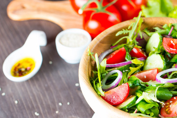 Fresh healthy salad with delicious ruccola, spinach, cabbage, arugula, feta cheese, red onion, cucumber, sesame seeds and cherry tomato on wooden background. Healthy and diet food concept.