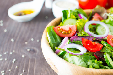 Fresh healthy salad with delicious ruccola, spinach, cabbage, arugula, feta cheese, red onion, cucumber, sesame seeds and cherry tomato on wooden background. Healthy and diet food concept.