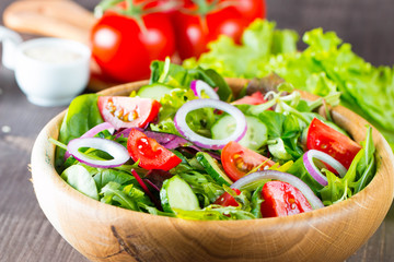 Fresh healthy salad with delicious ruccola, spinach, cabbage, arugula, feta cheese, red onion, cucumber, sesame seeds and cherry tomato on wooden background. Healthy and diet food concept.