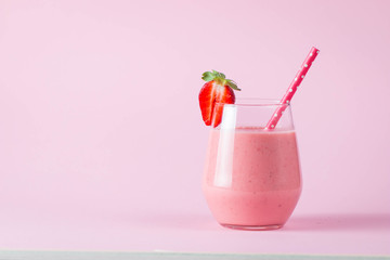 Glass of fresh strawberry milkshake, smoothie and fresh strawberries on pink, white and wooden background. Healthy food and drink concept.