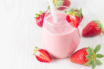Glass of fresh strawberry milkshake, smoothie and fresh strawberries on pink, white and wooden background. Healthy food and drink concept.