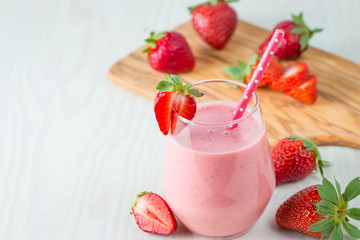 Glass of fresh strawberry milkshake, smoothie and fresh strawberries on pink, white and wooden background. Healthy food and drink concept.