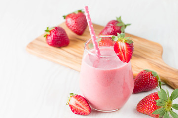 Glass of fresh strawberry milkshake, smoothie and fresh strawberries on pink, white and wooden background. Healthy food and drink concept.