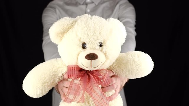 Young man in grey shirt gives a gift soft toy bear on black background. Congratulate Happy New Year, Merry Christmas, Happy Valentine's Day, presents gifts