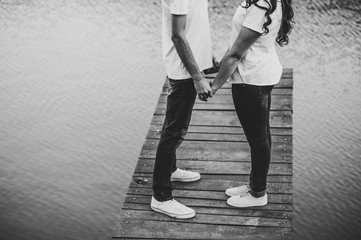 Young lovers pair, held of hands on a wooden bridge near lake. Rear view of couple standing on pier. lower half. Place for text and design. Close Up. Black and white photo.