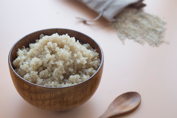  cooked quinoa in bowl and wooden spoon on brown background