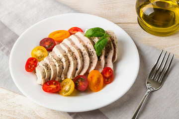 Juicy chicken breast cooked under vacuum at low temperature. Sliced chicken fillet and halves of fresh cherry tomatoes on a white plate. Low calorie diet food.