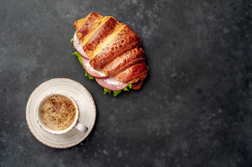 coffee and croissant - a sandwich with sausage and cheese on a cutting board on a stone background with copy space for your text